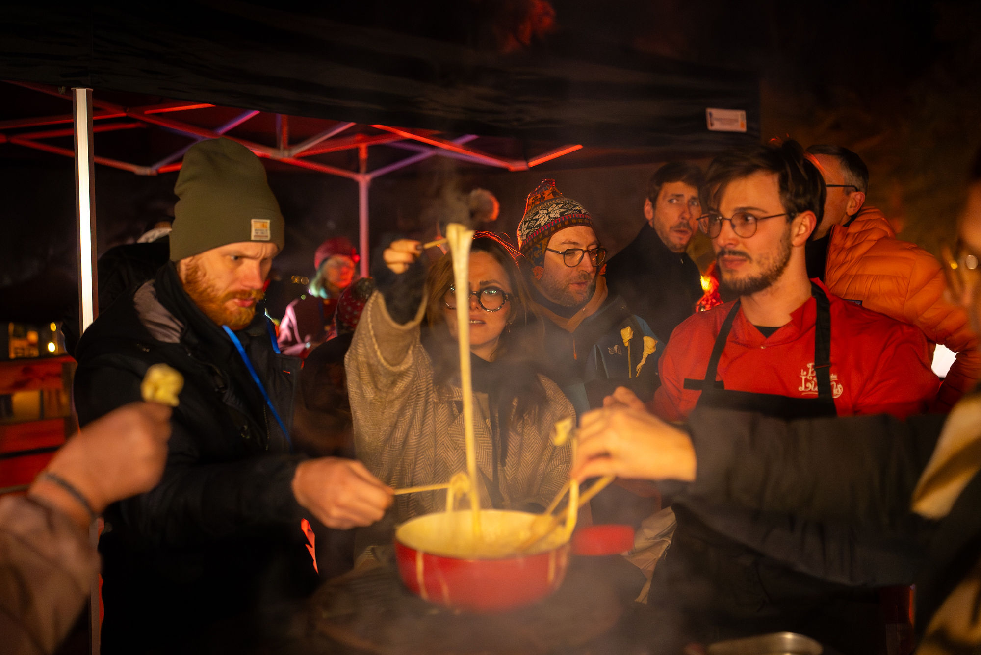 Des visiteurs en manteaux d’hiver partagent une fondue montagnarde lors des Fééries Nocturnes au Bois des Lutins